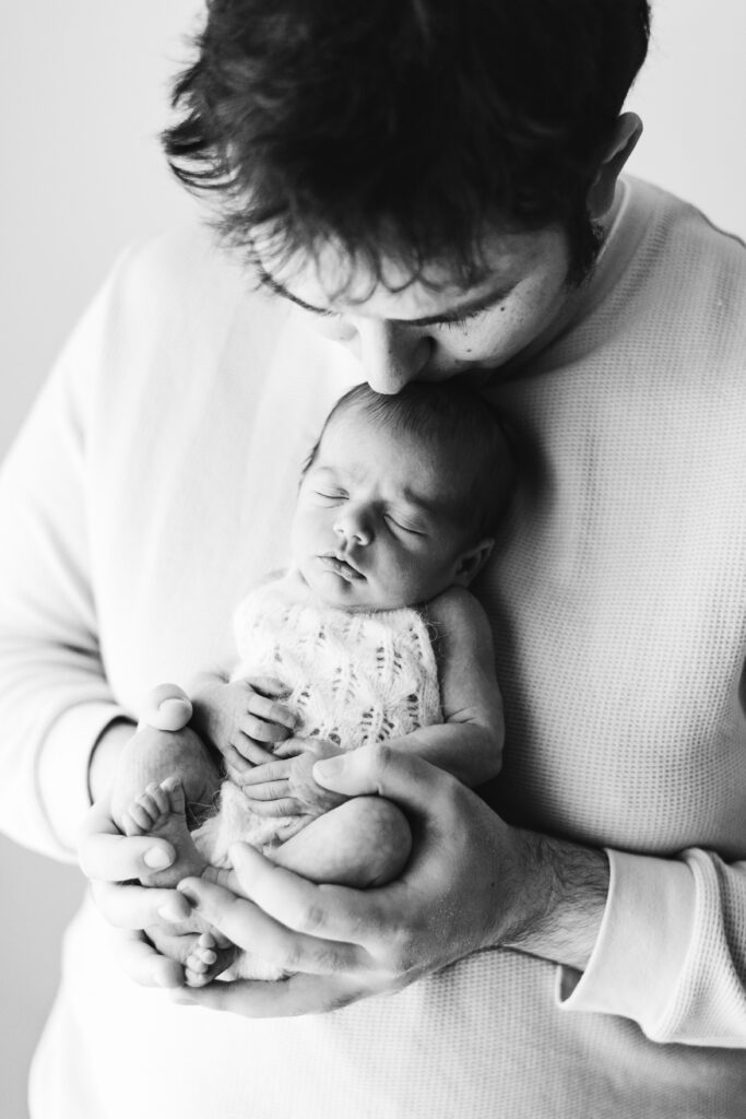 Dad kissing his baby daughter on the head whilst she sleeps at Billingshurst newborn photoshoot