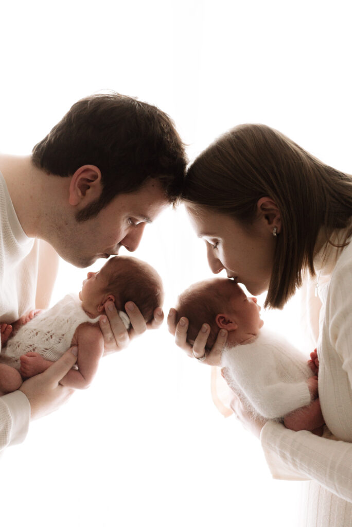 Mum and dad kissing their newborn twins on the head during a newborn photoshoot in Billingshurst