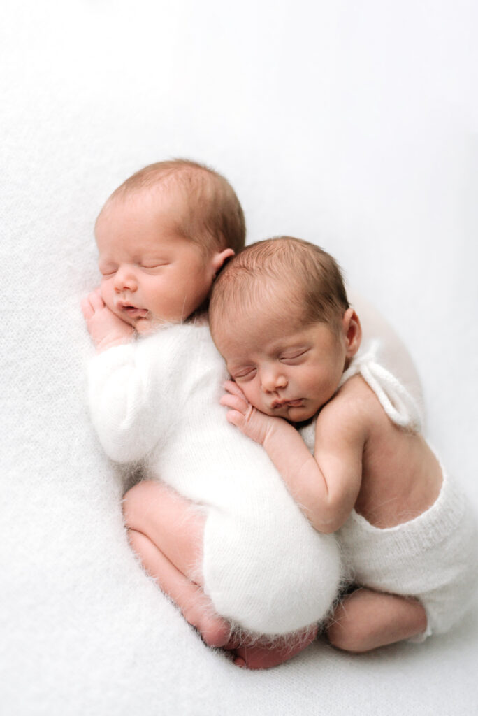 Twin newborns sleeping and laying ontop of eachtoher at a photoshoot in Billingshurst