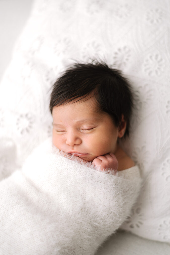 Baby girl wrapped in a white blanket sleeping in newborn photoshoot in Billingshurst