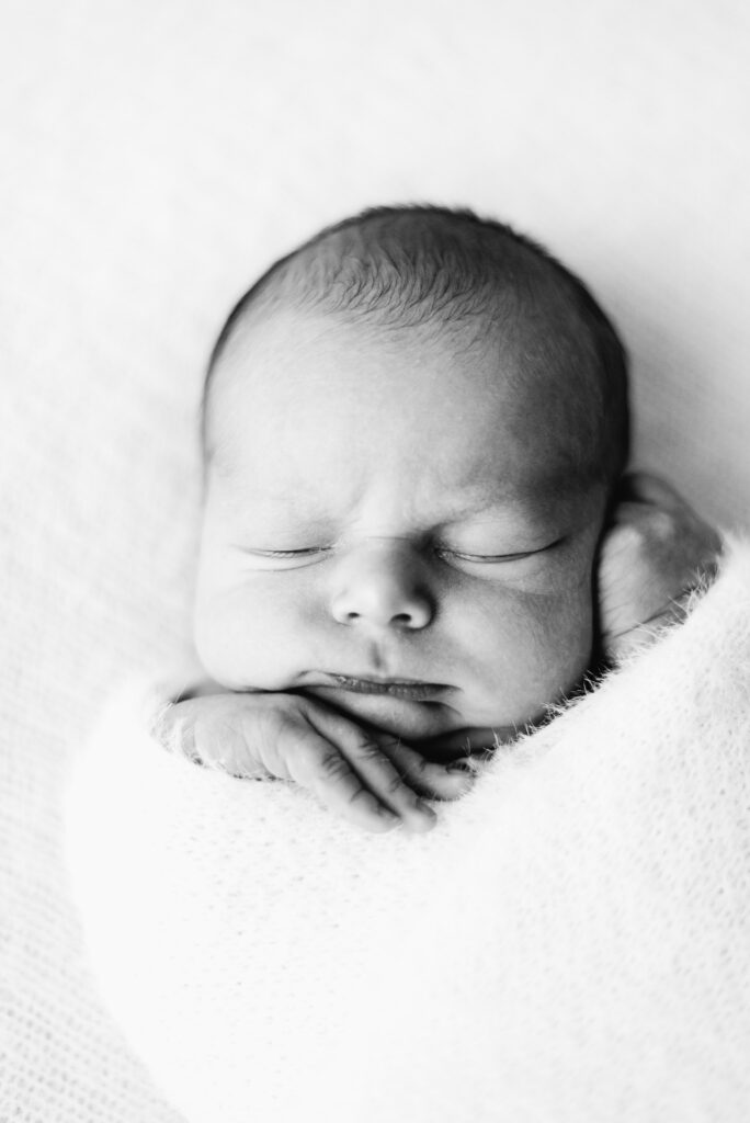 Baby boy sleeping wrapped up in a white blanket at West Sussex newborn photoshoot