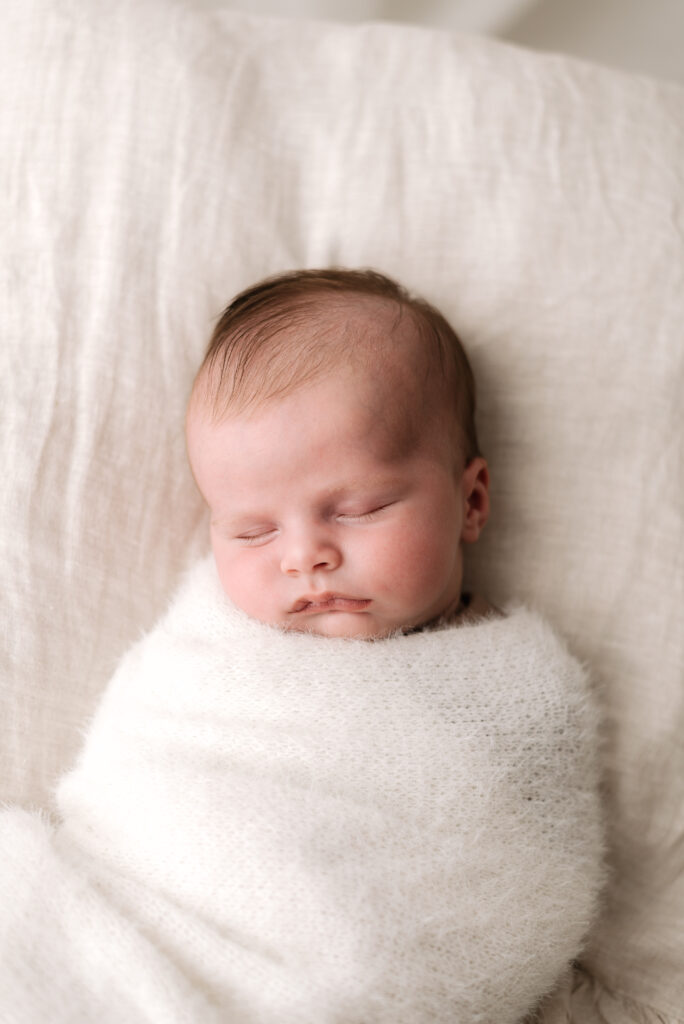 A newborn baby boy swaddled up in a blanket sleeping at a newborn photoshoot in Horsham