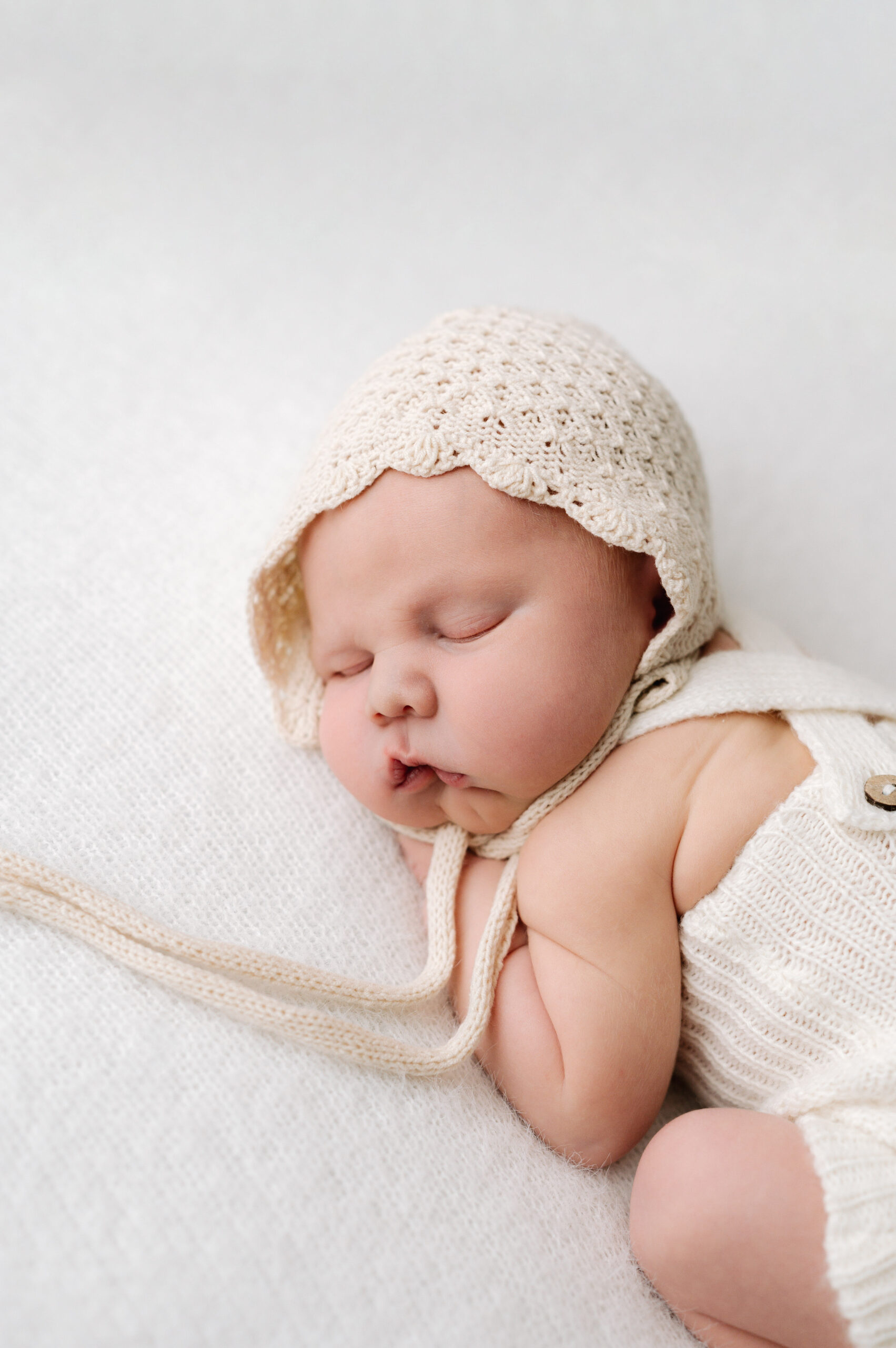 Baby boy sleeping on a white blanket with a hat on during a Natural newborn photoshoot in Horsham