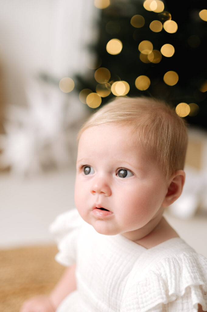 A baby girl sitting infront of a christmas tree at a christmas photoshoot in West Sussex