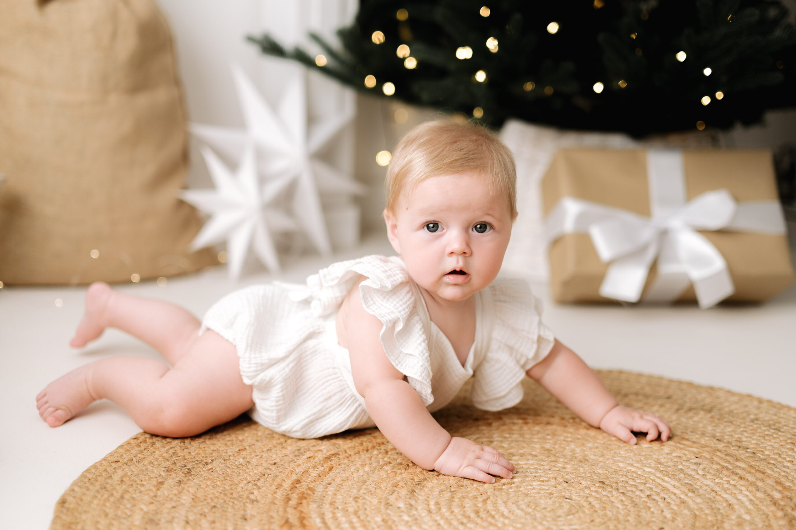 1 year old baby laying down on a brow rug in front of a christmas tree at Billingshurst family photoshoot