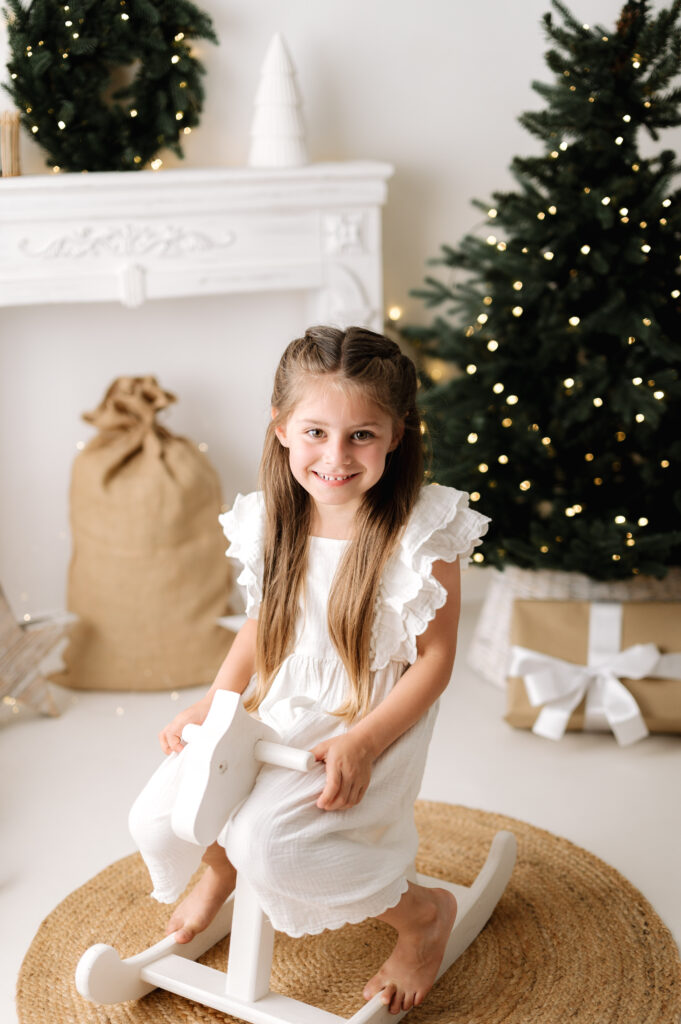 A girl sitting on a white rocking horse smiling during a Christmas photoshoot in West Sussex