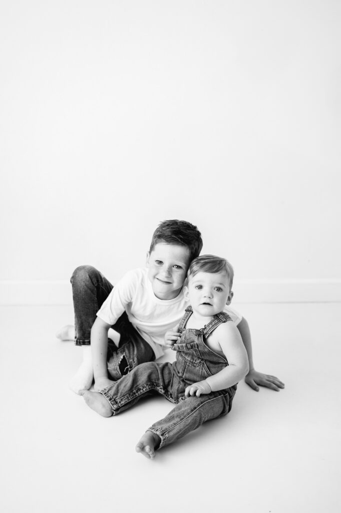 A one year old boy sitting on the floor with his big brother at a photoshoot in Billingshurst
