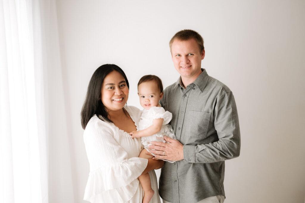 A family of 3 smiling in front of a white wall at Billingshurst family photoshoot