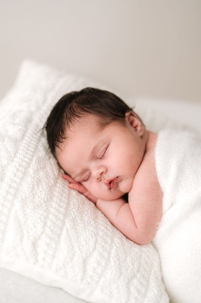 A newborn baby sleeping on a white pillow during a newborn photoshoot in Horsham, West Sussex