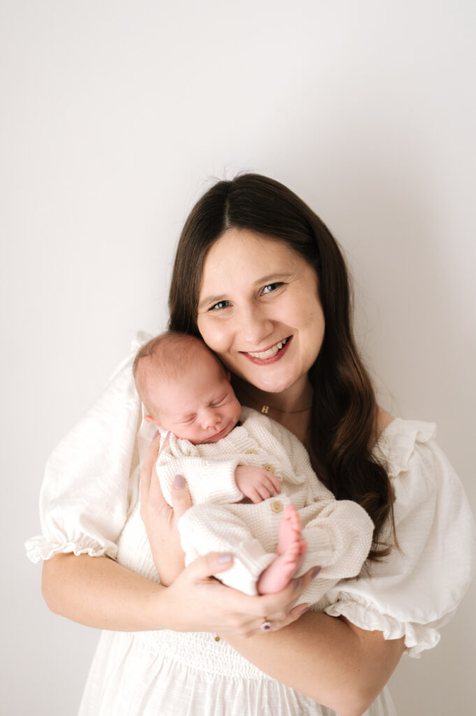 New mother holding her newborn son in her arms with a big smile at a photoshoot in Horsham