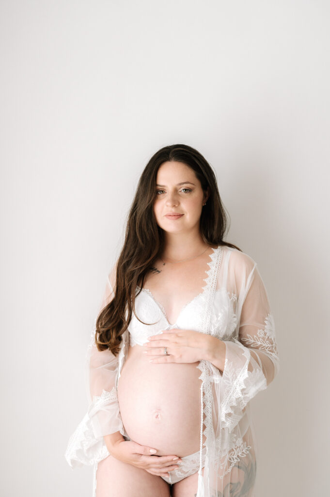 Pregnant mother holding her bump and smiling at a maternity photoshoot in Horsham