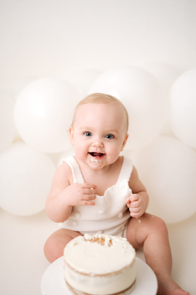 1 year old girl sitting down smiling whilst at her cake smash photoshoot in Horsham
